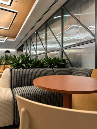 Modern restaurant interior with booth seating and a round table with an arrangement of interior plants in a plant bed behind the table.